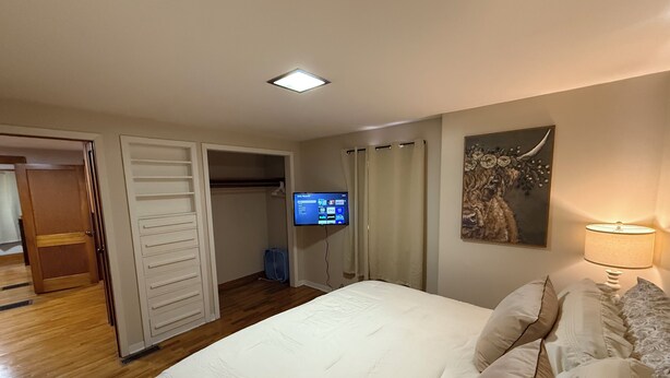 A bedroom with a bed, a TV mounted on the wall, a painting, and a lamp. - Cozy Corner Cottage - 4 Bed/2 Bath
No Cleaning Fee! (Salina)