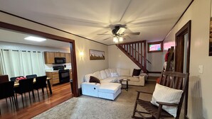 A spacious living area with a sofa, a dining table with chairs, a kitchen in the background, and a staircase leading upstairs. - Cozy Corner Cottage - 4 Bed/2 Bath
No Cleaning Fee! (Salina)