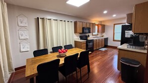 A compact kitchen with wooden cabinets, a microwave, a stove, and a dishwasher. There is a dining table with chairs and a bowl of fruit. - Cozy Corner Cottage - 4 Bed/2 Bath
No Cleaning Fee! (Salina)