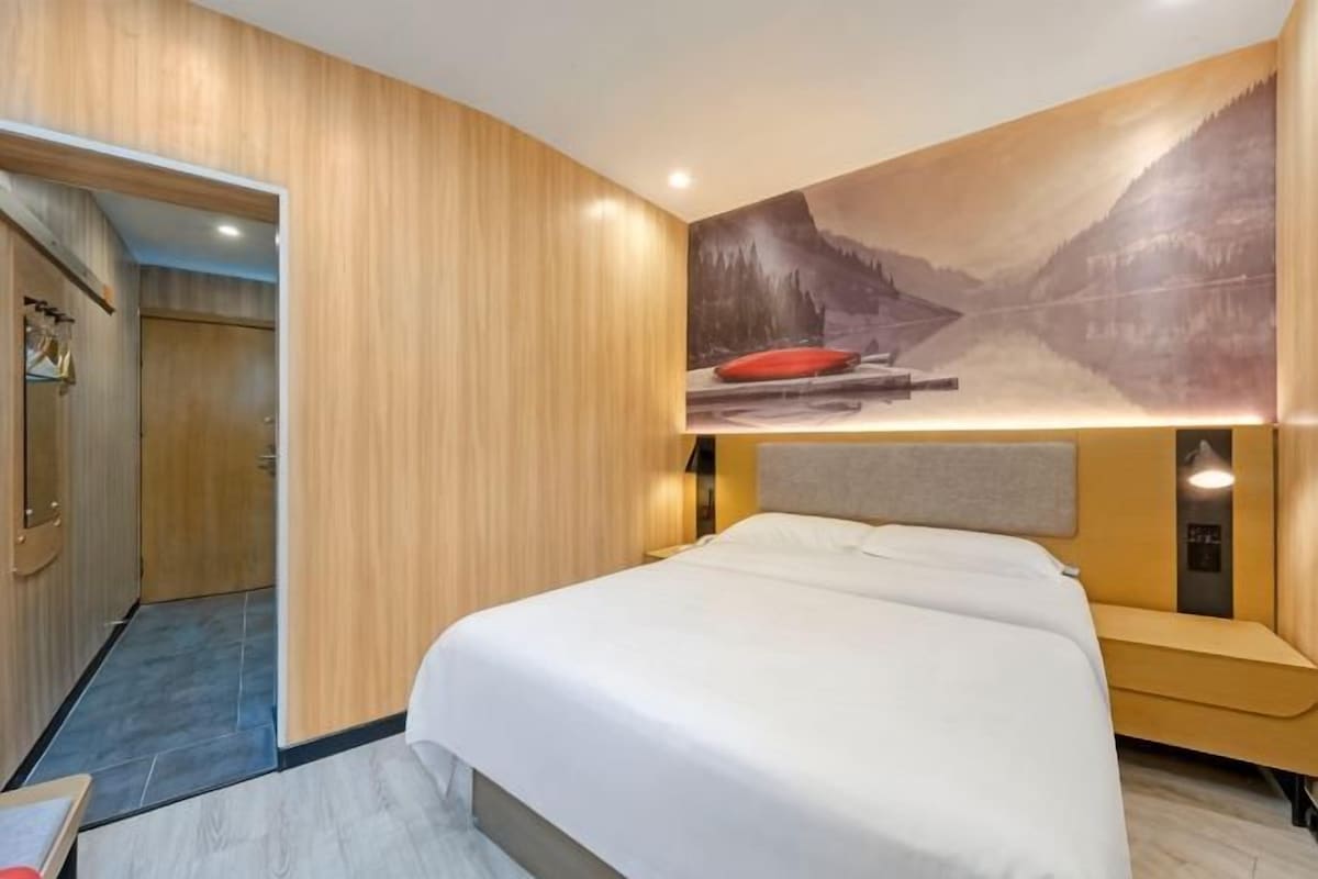 A hotel room with a bed, a headboard, a wall-mounted artwork, and a wooden wardrobe.