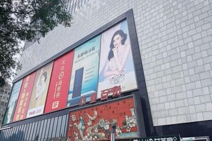 Fachada de edificio con varios anuncios, incluyendo un cartel rojo destacado y un cartel azul con una mujer.