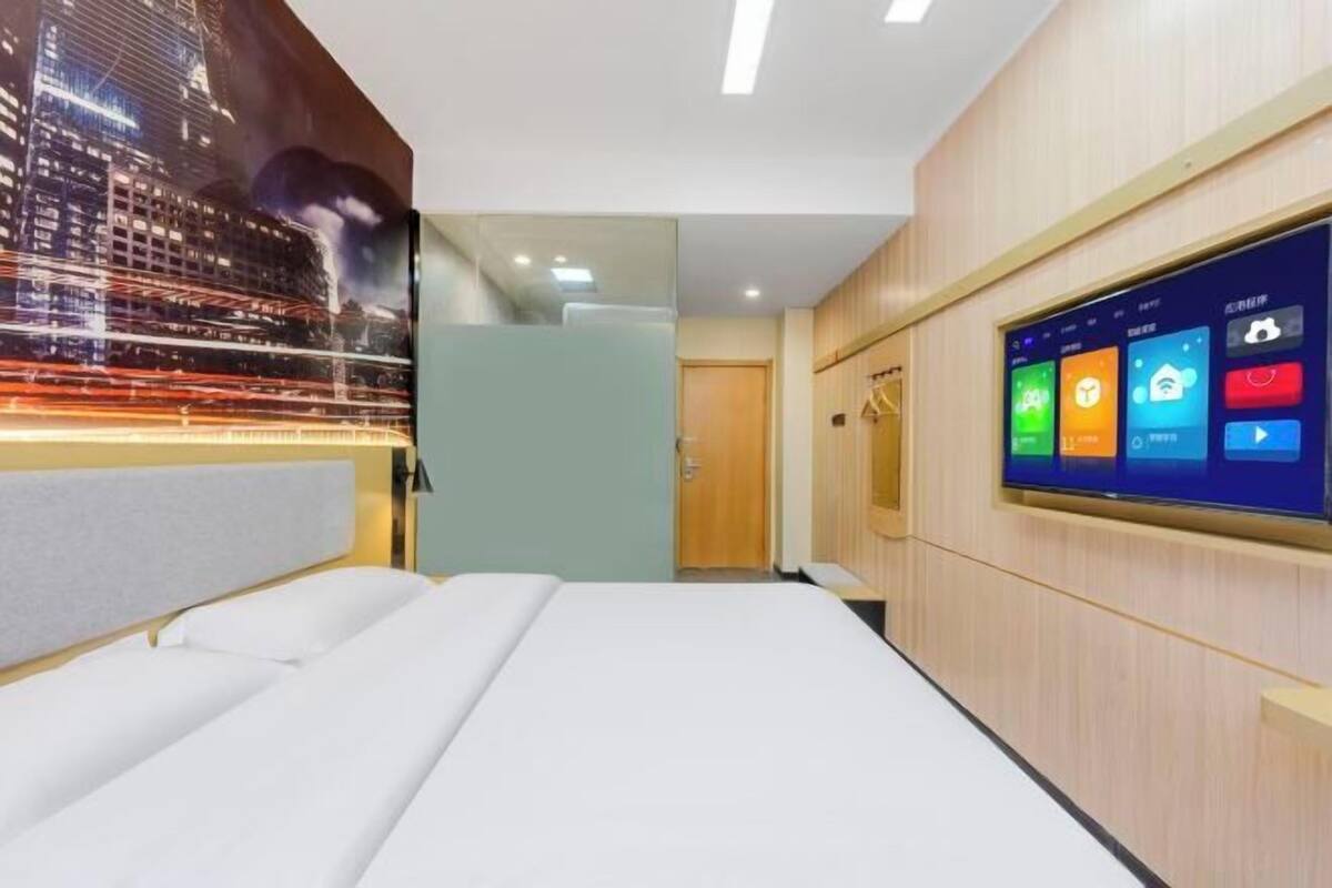 Habitación de hotel moderna con una cama grande, una pantalla digital que muestra los controles de la habitación y un mural con vistas a la ciudad.