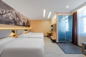 Habitación de hotel con tres camas, un escritorio, un televisor y una puerta de vidrio que da a un balcón.