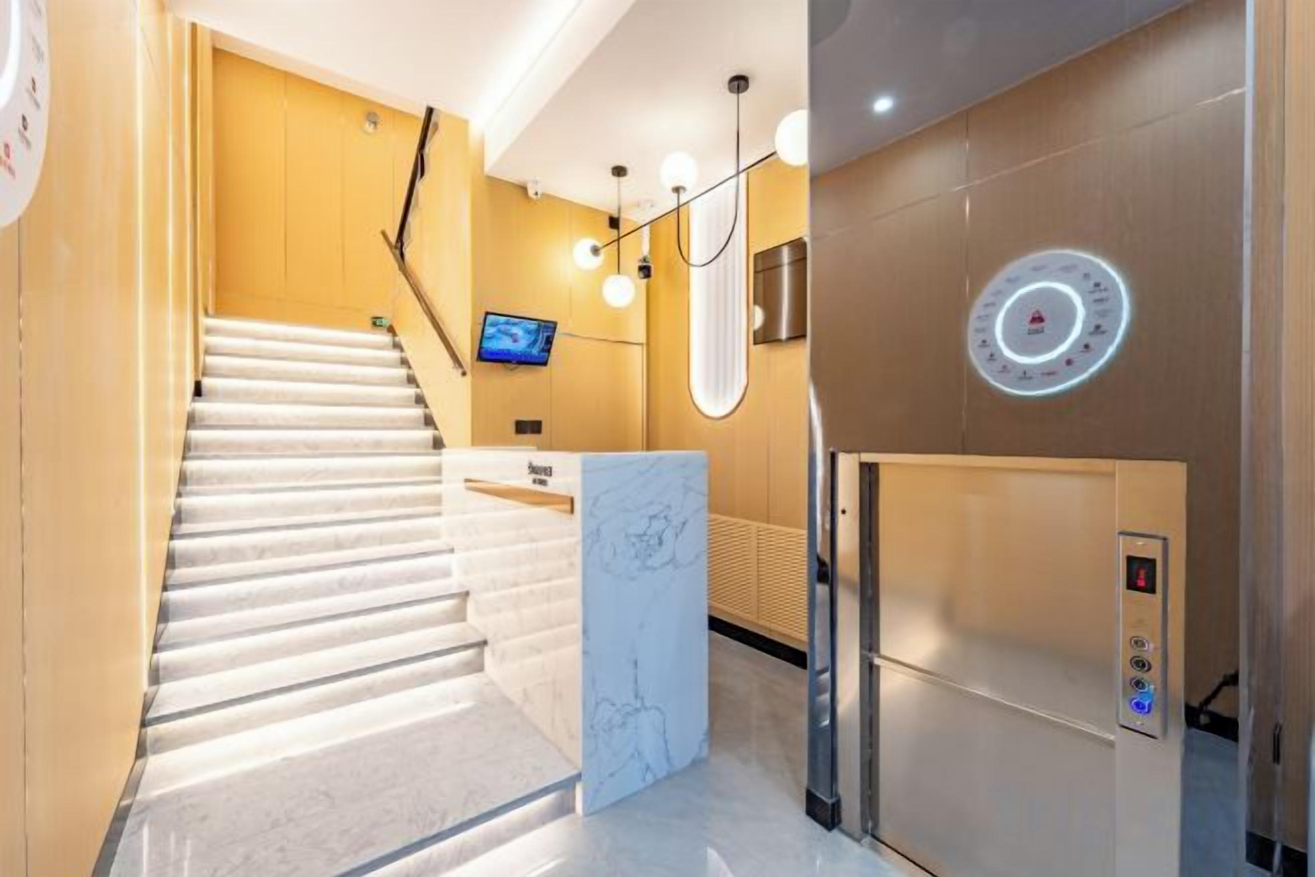A hotel lobby with a marble reception desk, a staircase, and a modern elevator.