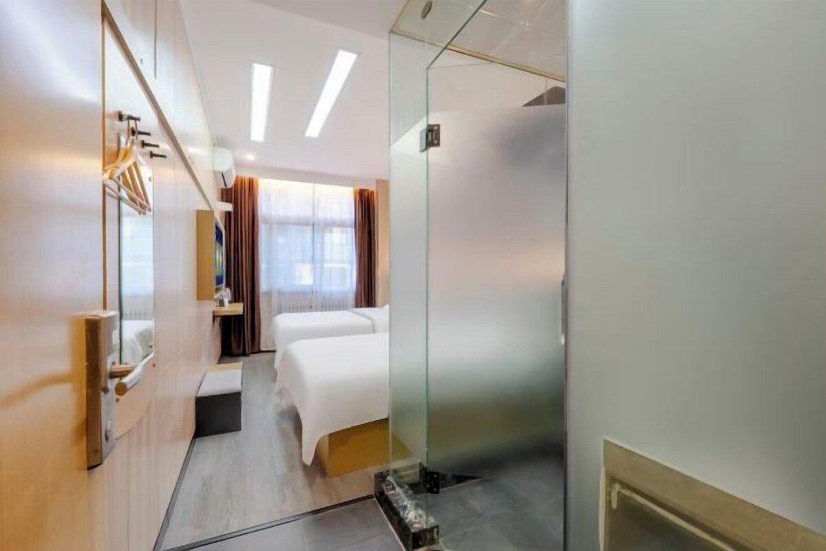 Ett hotellrum med en säng, en liten sittgrupp, en spegel och en glasvägg.