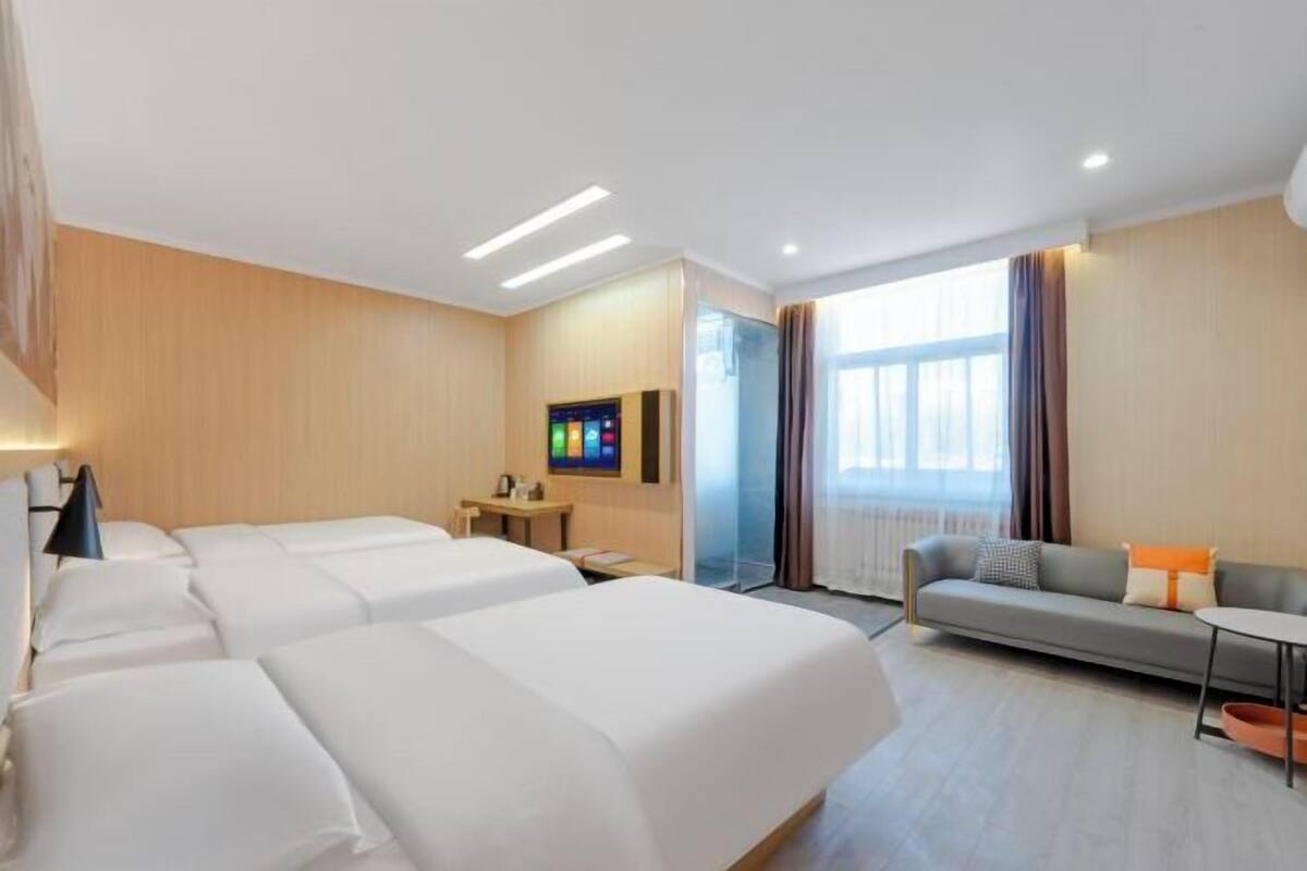 Habitación de hotel con dos camas, un sofá, una mesita, un televisor y una ventana con cortinas.
