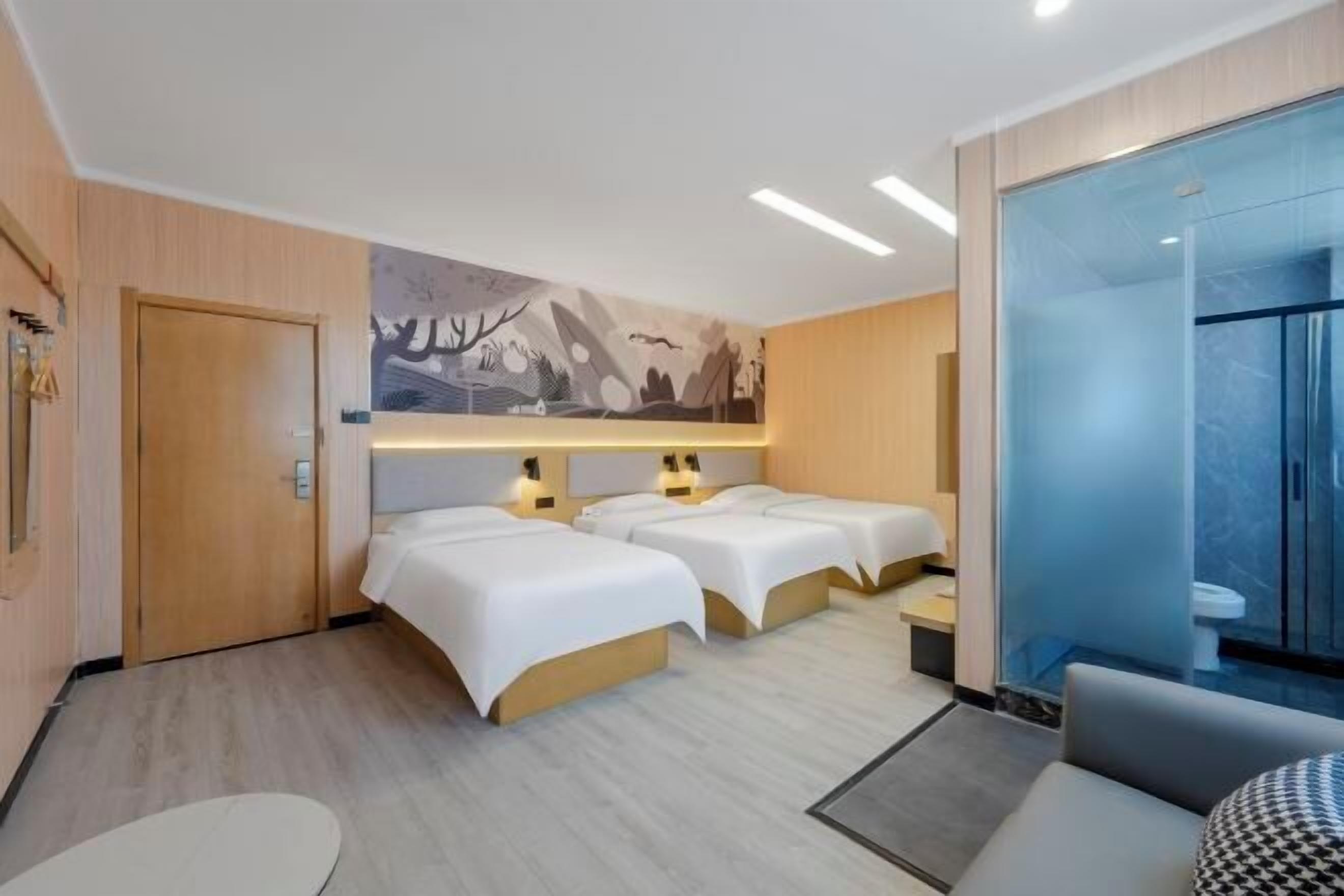 Ein Hotelzimmer mit zwei Betten, einem Schlafsofa, einem kleinen Tisch und einem Badezimmer mit einer Duschkabine.