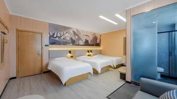 Ein Hotelzimmer mit zwei Betten, einem Schlafsofa, einem kleinen Tisch und einem Badezimmer mit einer Duschkabine.