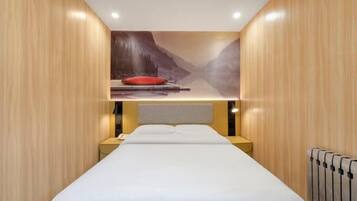 Ein Hotelzimmer mit Bett, Nachttisch, rotem Kopfkissen und Wandgemälde einer Berglandschaft.