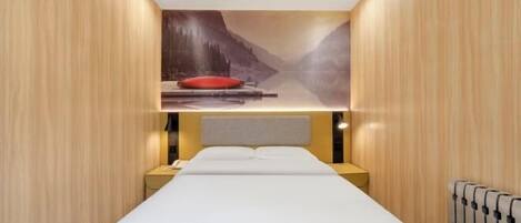 Habitación de hotel con cama, mesita de noche, almohada roja y un mural en la pared con un paisaje de montaña.