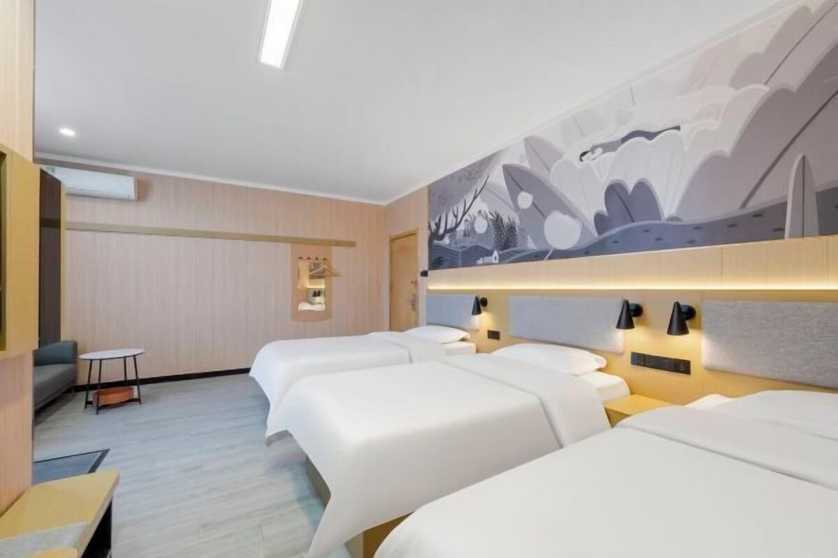 Ett hotellrum med tre sängar, en soffa, ett litet bord och ett konstverk som hänger på väggen.