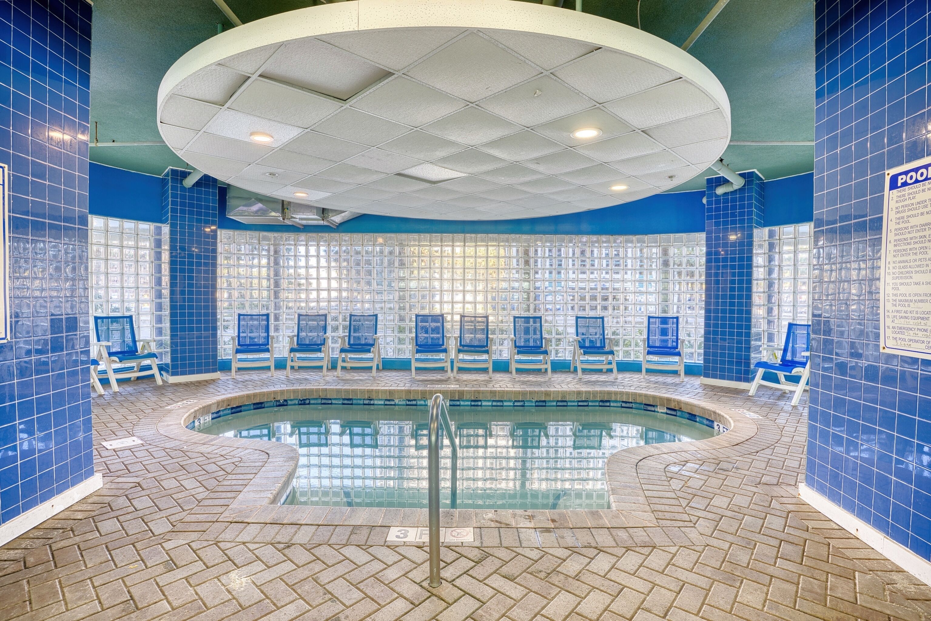 An indoor swimming pool with blue tiled walls, a circular ceiling, and lounge chairs around the pool.
