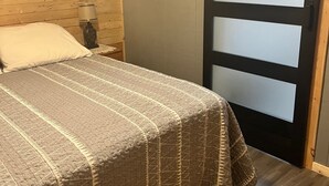 Ein Schlafzimmer mit Bett, Nachttisch, Lampe, einem Bild an der Wand und einer Schiebetür.