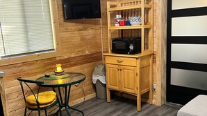 Ein kompaktes Wohnmobil-Interieur mit Holzausstattung, einem Esstisch mit Stühlen, einer Mikrowelle, einem kleinen Schrank und einem an der Wand befestigten Fernseher.
