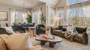 A spacious living room with a large window, a dining area, and a cozy seating arrangement. - 4k SqFt, Massive Deck , Games, Spa, Sauna, Firepit (Hendersonville)