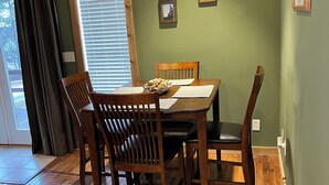 A dining area with a wooden table and chairs, a window with blinds, and two small wall-mounted picture frames. - Charming 1-bedroom house in Paris, TN. (Paris)