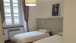 Un dormitorio con dos camas, un radiador, una ventana con cortinas y un cuadro en la pared.