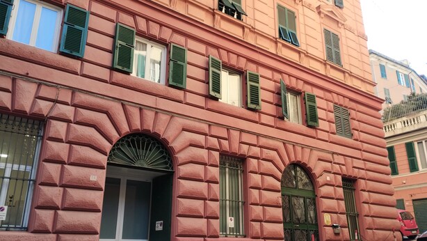 Un edificio rosa con contraventanas verdes, una puerta y un ventanal con arco decorativo.