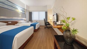 Ein Hotelzimmer mit zwei Betten, einem Schreibtisch, einem Stuhl, einem Fernseher und einer Pflanze.