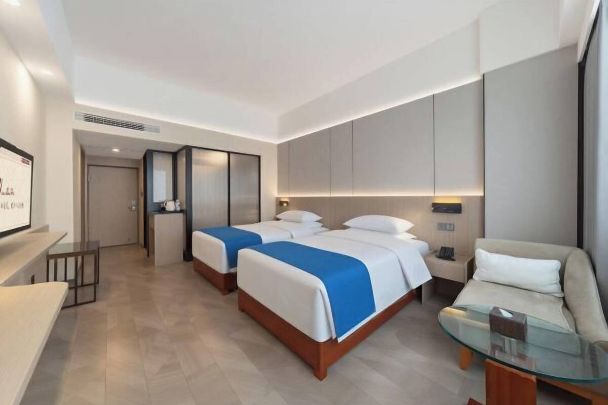 A hotel room with two beds, a sofa, a glass coffee table, and a TV.