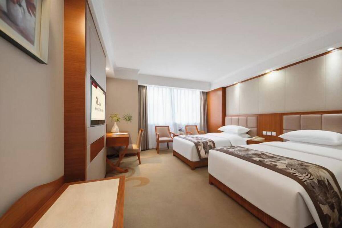 A hotel room with two beds, a desk, a chair, and a large window with curtains.