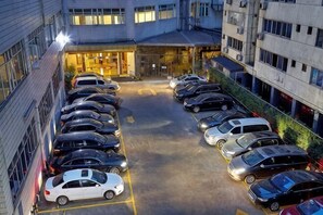 Um estacionamento com vários carros, entrada de um edifício e visão ampla da área.