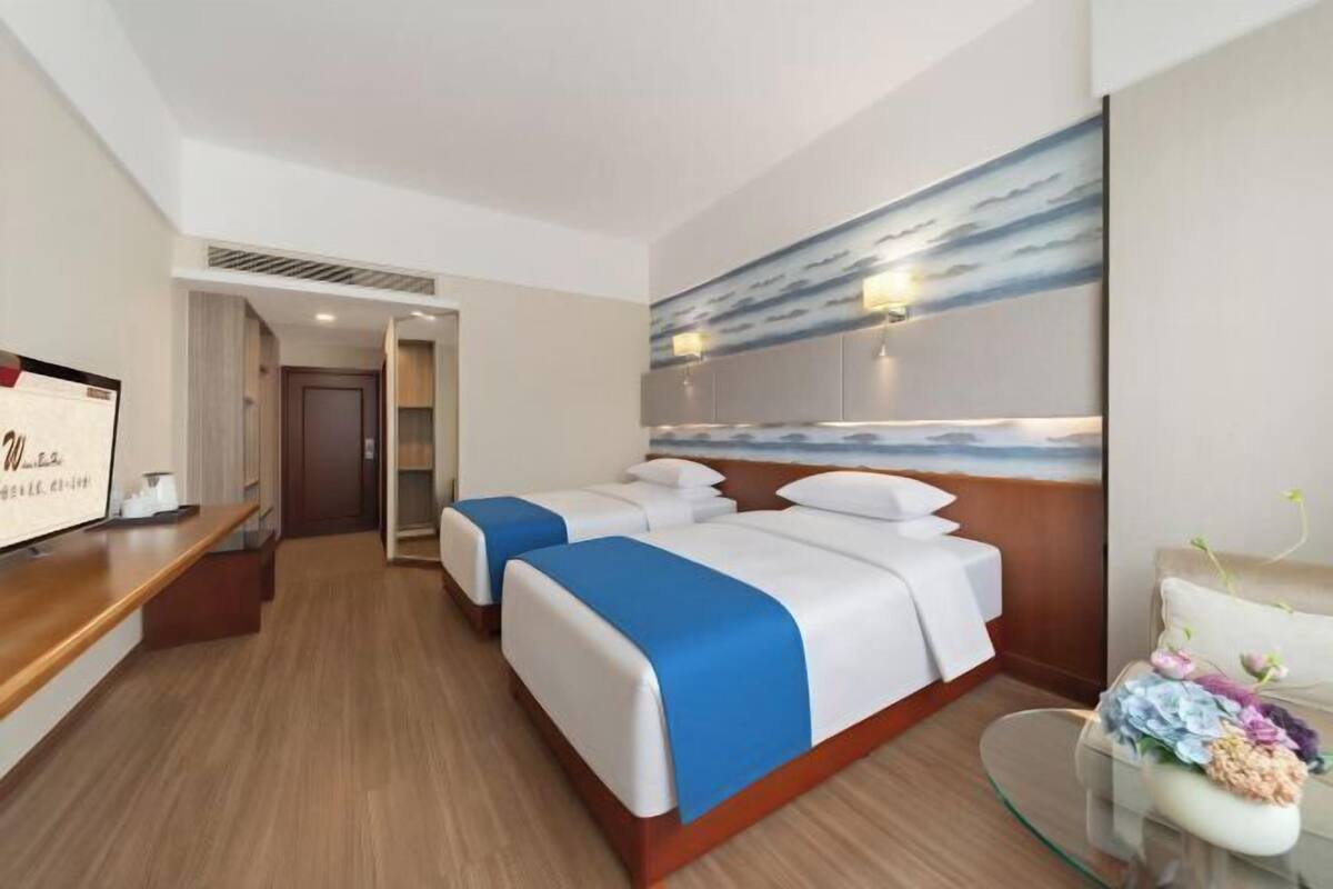 A hotel room with two beds, a desk, a chair, and a painting on the wall.