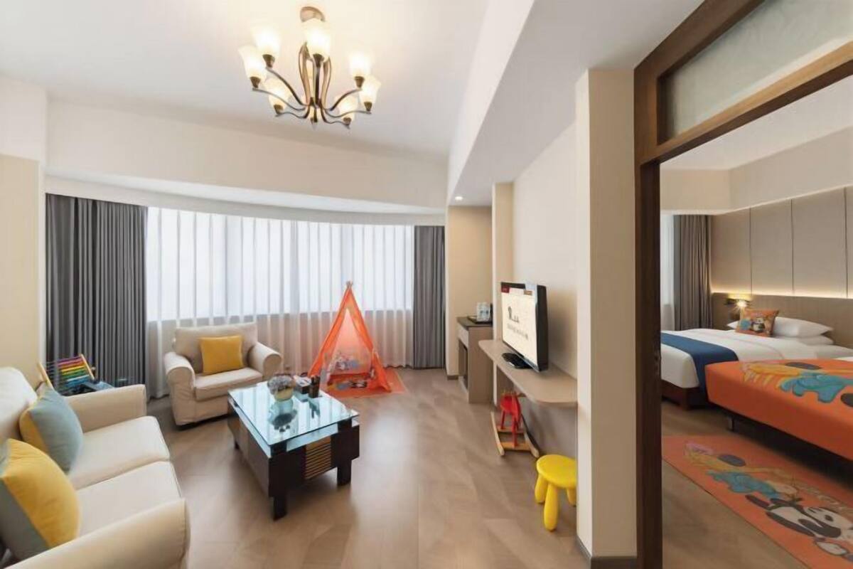 A hotel room with a sofa, a coffee table, a TV, a bed, and a window with curtains.