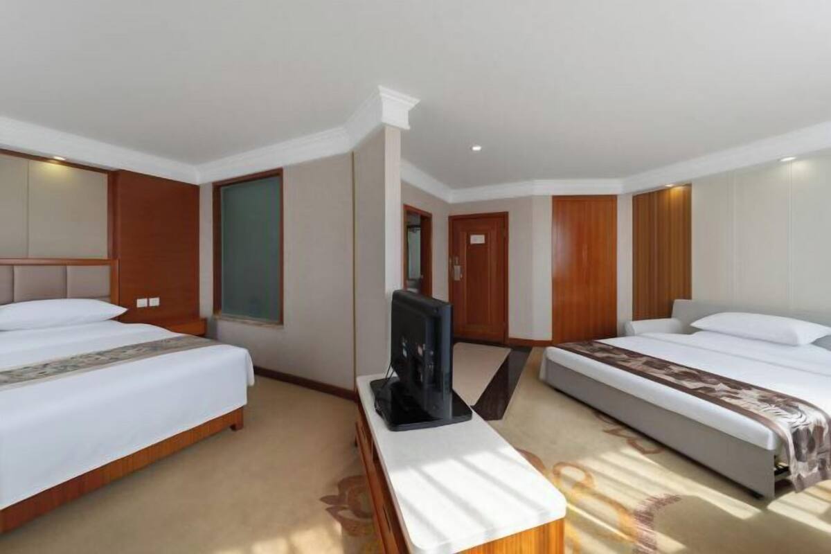A hotel room with two beds, a television on a stand, and a large mirror.