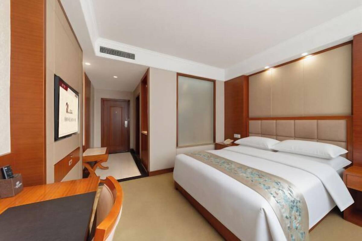 A hotel room with a bed, bedside table, and a desk with a chair.