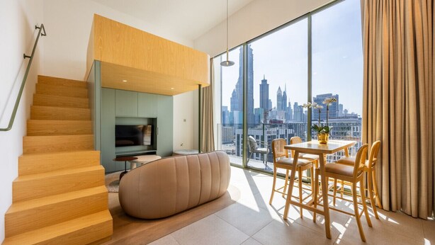 Un salon moderne avec un escalier en bois, un canapé, une table à manger avec des chaises et une grande fenêtre donnant sur la ville.