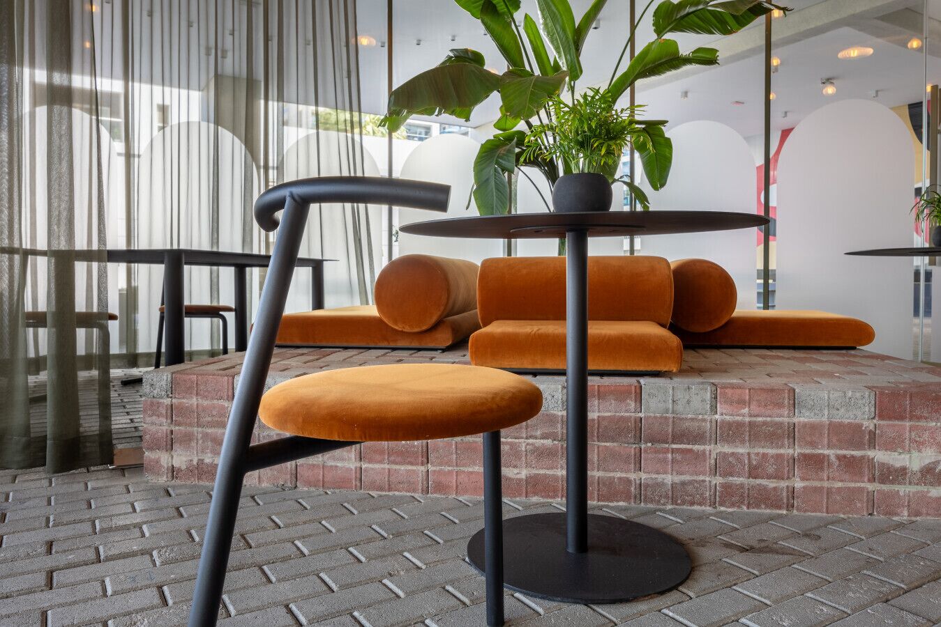 Un espace détente avec des coussins orange et une table ronde, une plante en pot et une chaise au dossier incurvé.