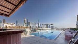 A rooftop pool with a city skyline view, a covered seating area, and a modern architectural design. - Mood 45 - Deluxe Studio: Chic with private Terrace (Jumeirah Garden City)