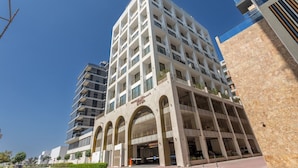A multi-story hotel with a modern architectural design, featuring a central courtyard with arches and a parking garage below. - Mood 45 - Deluxe Studio: Chic with private Terrace (Jumeirah Garden City)