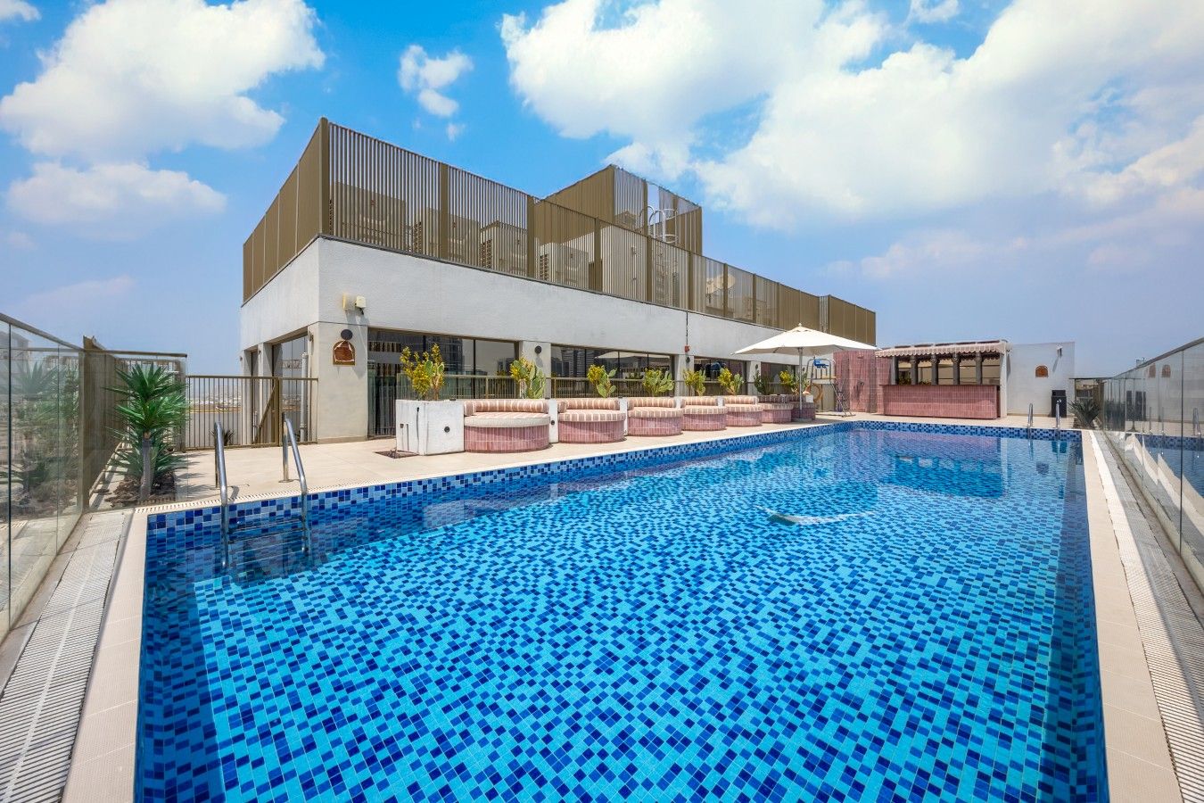 Une piscine dot ée d’une terrasse carrelée, d’un espace salon couvert et d’un bâtiment moderne avec de grandes fenêtres.