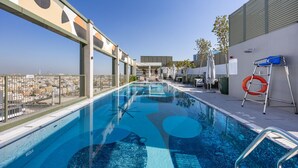 Una piscina en la azotea con agua azul cristalina, rodeada por una cerca de metal y un flotador salvavidas a la derecha.