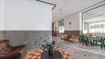 A modern lobby with a checkered floor, a brown sofa, a round table, and green chairs.