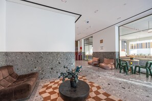 A modern lobby with a checkered floor, a brown sofa, a round table, and green chairs. - Mood 45 - Deluxe Studio: Your Perfect Getaway (Jumeirah Garden City)