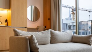 A modern living room with a beige sofa, a round mirror, and a view of a construction site through large windows.