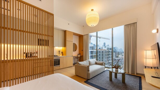 A modern hotel room with a large bed, a sofa, a dining area, and a view of the city skyline.