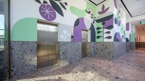 Un área de ascensor moderna con suelo de terrazo y un mural abstracto de colores en las paredes.
