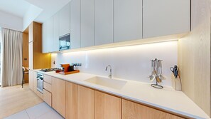 Une cuisine moderne avec un plan de travail blanc, des armoires en bois, un four encastré et un évier en acier inoxydable.