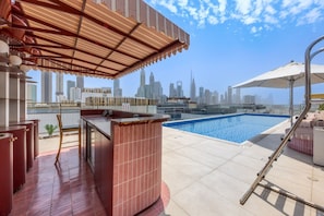Une piscine sur le toit offrant une vue panoramique sur la ville, un bar et des espaces de détente en plein air.