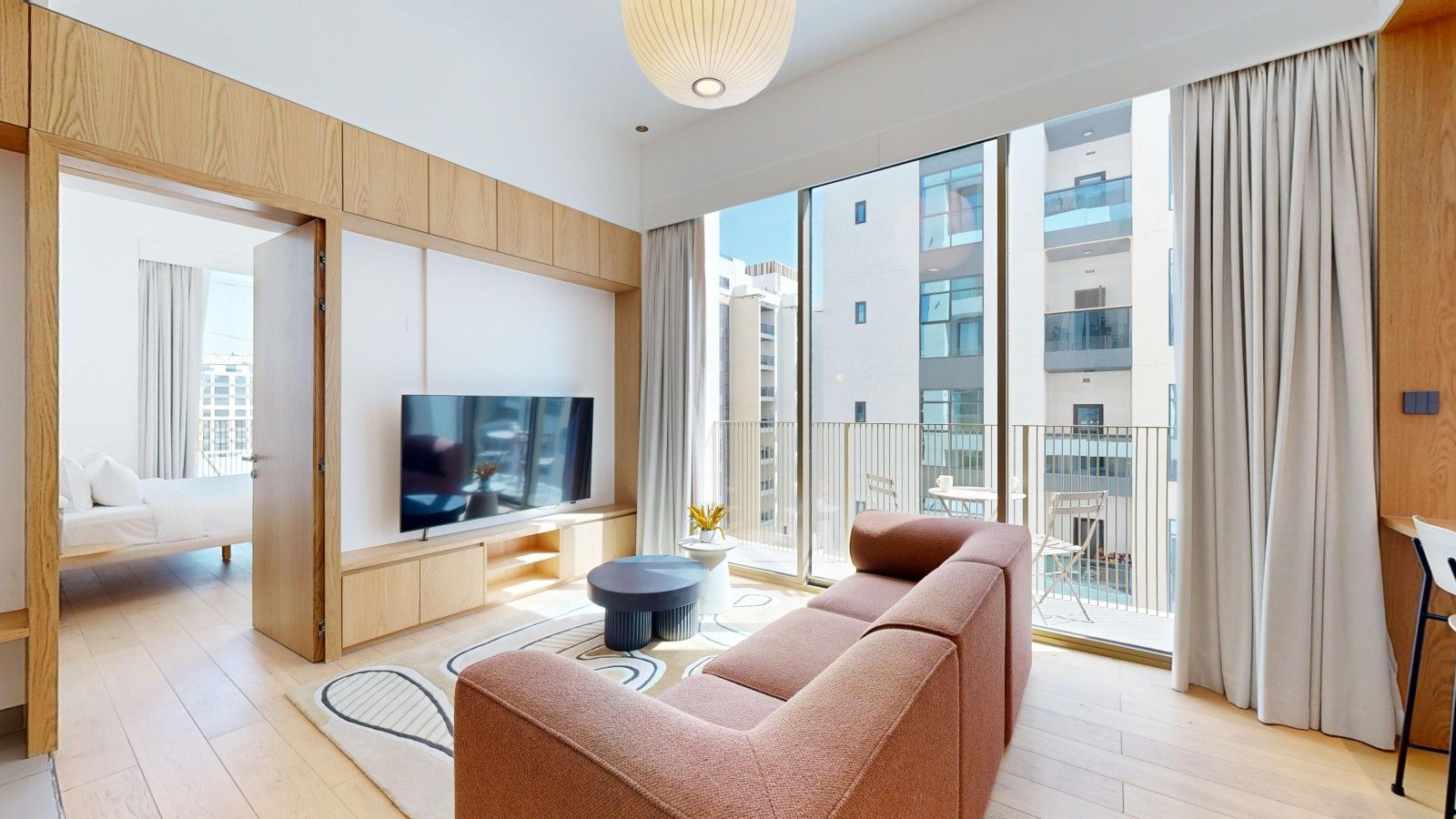 A modern living room with a sofa, a TV, and a balcony with curtains.
