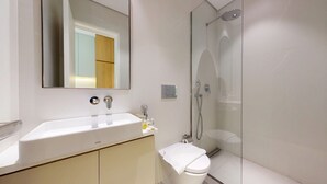 Un baño moderno con lavamanos blanco, espejo y ducha con mampara de vidrio.