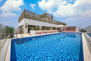 A swimming pool with a tiled deck, a covered seating area, and a modern building with large windows. - Mood 45 - Two Bed: Elegant & luxurious (Jumeirah Garden City)