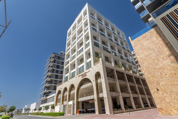 A multi-story hotel with a modern architectural design, featuring a central courtyard with arches and a parking garage below.