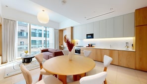 Une cuisine moderne avec des meubles blancs, un coin repas doté d’une table ronde et un espace de vie comprenant un canapé et une vue sur la ville.