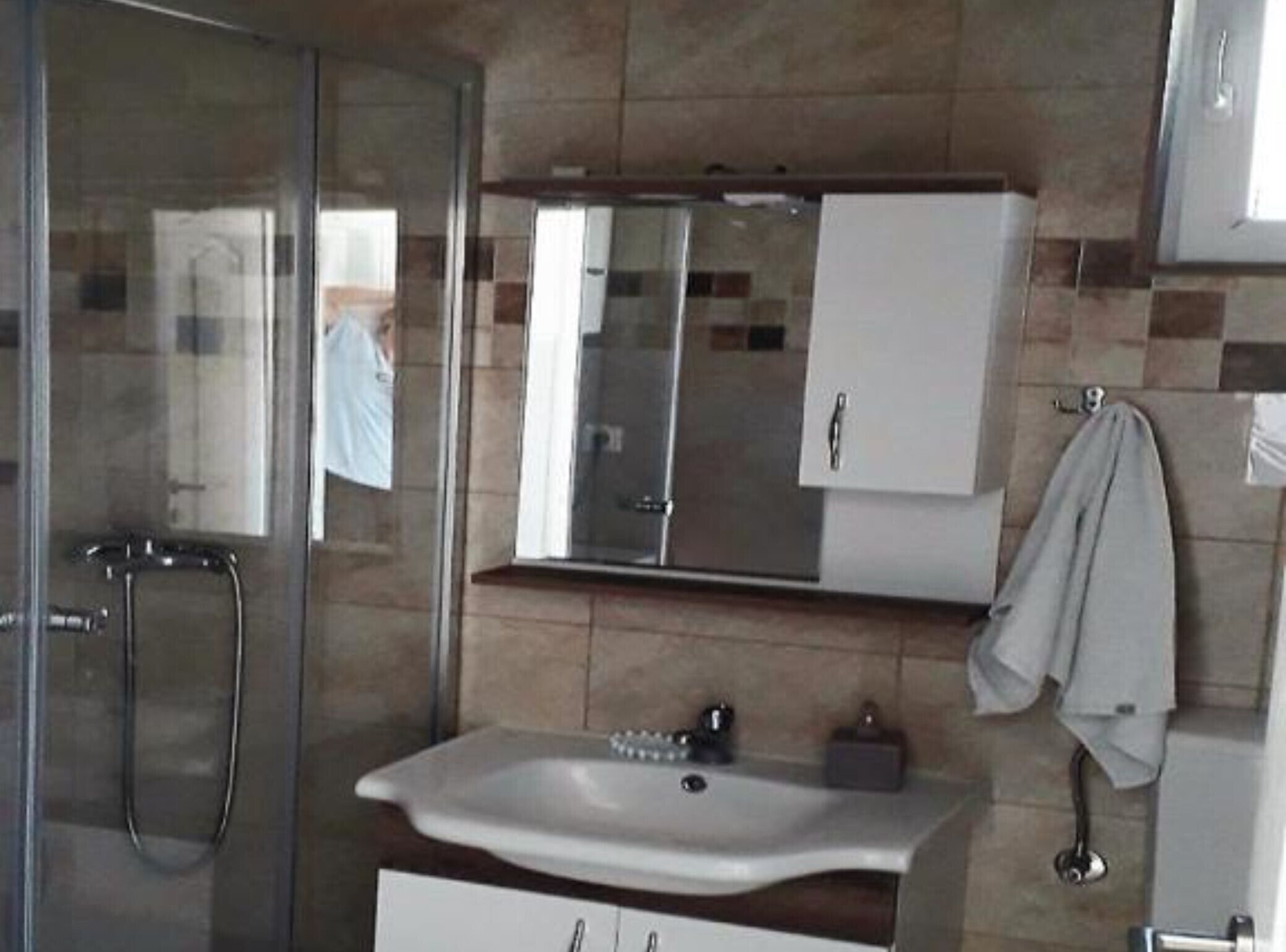 Un bagno con box doccia in vetro, un lavandino con specchio sopra e un asciugamano su un portasciugamani.