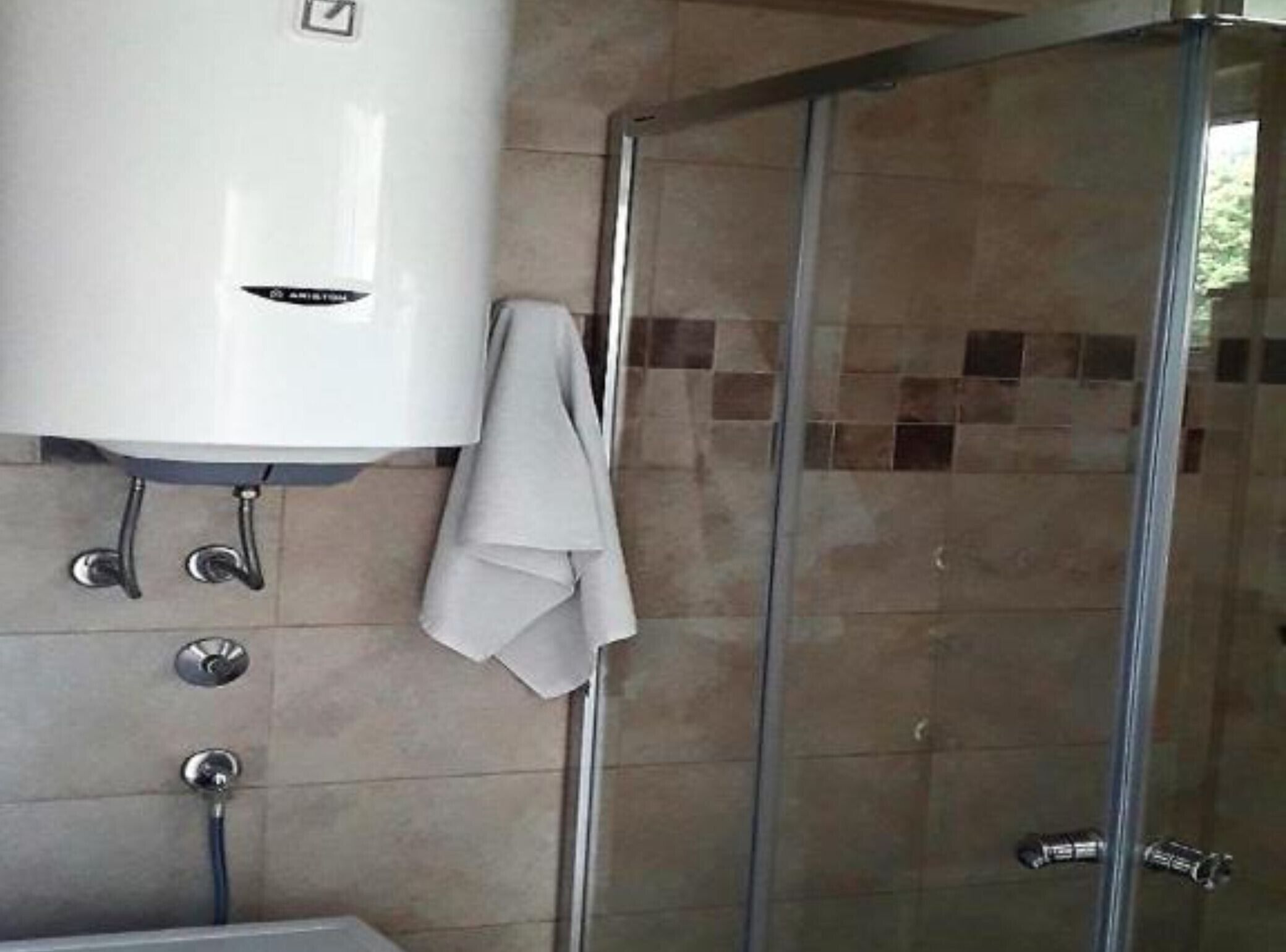 Une salle de bain avec un chauffe-eau blanc, une cabine de douche en verre et des murs carrelés.